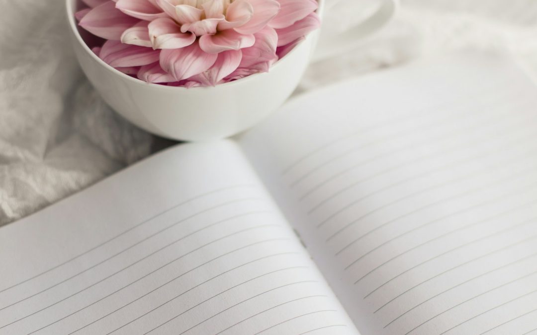 A cup of herbal tea with a pink flower beside an open journal, symbolizing calm root-cause self-care for hormonal health.