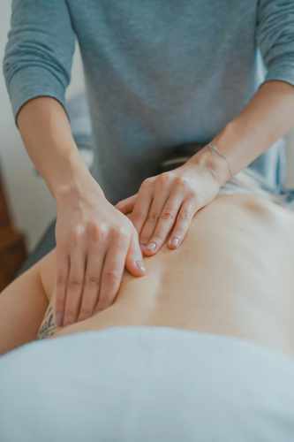 Massage therapist performing deep tissue work on a client's shoulder and upper back, illustrating sports massage therapy for muscle recovery