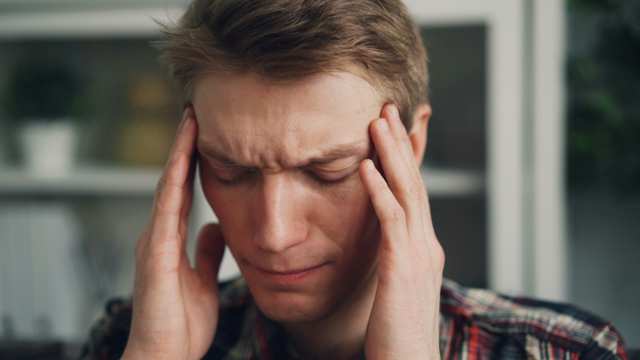 Man rubbing his temples with both hands, eyes closed in discomfort from a tension headache