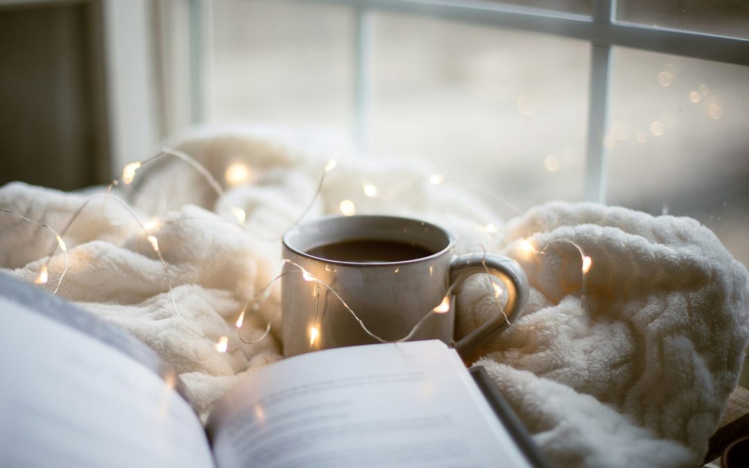 A cup of coffee and an open book resting on a soft blanket, a cozy way to spend a dark autumn day
