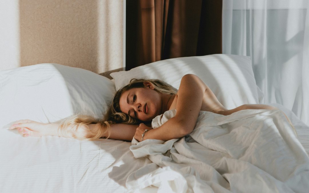 Woman resting peacefully in a bright bed with white linens, representing better sleep during perimenopause